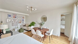 Un salon moderne avec un coin repas, comprenant une table ronde en bois, des chaises blanches, un canapé et un grand miroir.