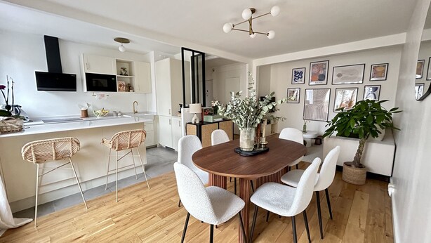 Une cuisine moderne avec des meubles blancs, une table à manger en bois avec des chaises blanches et un coin bar avec des chaises en osier.