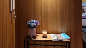 A wooden room with a bedside table holding a book, a candle, and a vase of flowers. - Fervença Apartments - Sabor (Vila Nova de Gaia)