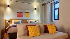 A modern hotel room with a sofa, a bed, a wooden headboard, and artwork on the wall. - Fervença Apartments - Sabor (Vila Nova de Gaia)