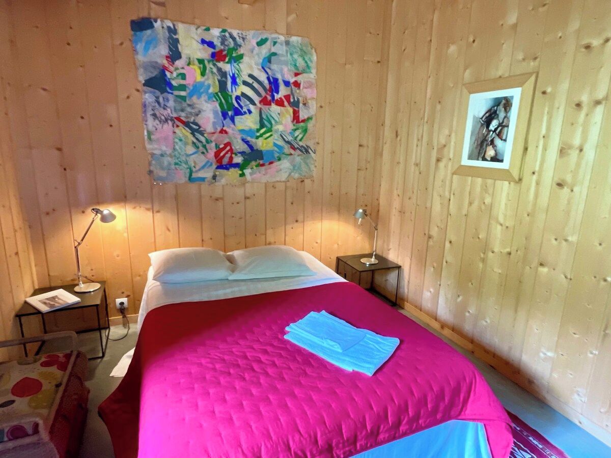 A room with a bed, a bedside table, a lamp, and a wall painting.