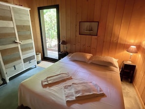A wooden-paneled room with a bed, a wardrobe, and a small table with a lamp.