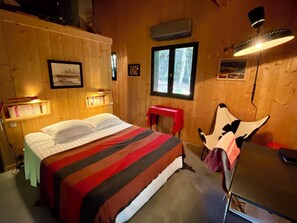 Relax in this serene bedroom with a large bed, desk, and window offering a view of the surrounding trees.