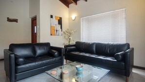 A living room with two black leather sofas, a glass coffee table, and a window with blinds.