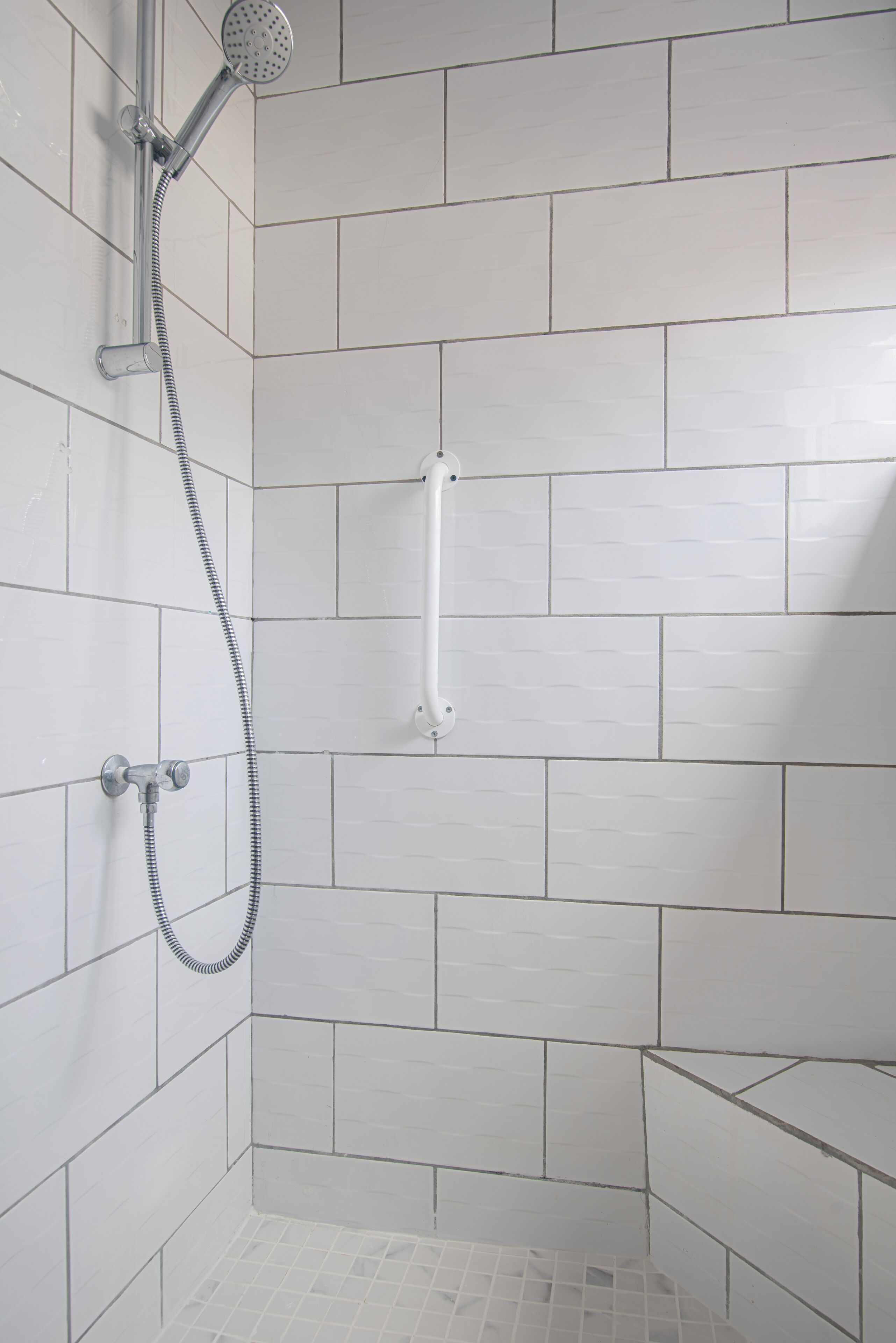 Un espacio de ducha con azulejos blancos, un cabezal de ducha manual y una manguera de ducha.