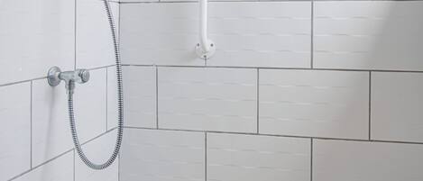 Un espacio de ducha con azulejos blancos, un cabezal de ducha manual y una manguera de ducha.