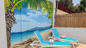 A beach-themed mural with two white lounge chairs and a bamboo fence.