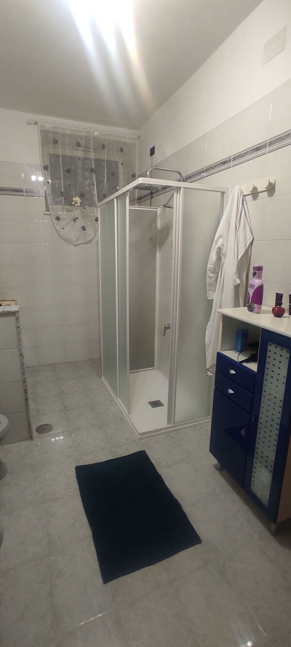 A bathroom with a glass-enclosed shower, a white sink, a blue cabinet, and a black rug on the floor. - 2 Bedroom Apartment in Campania (Campania)