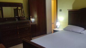 A bedroom with a wooden dresser, a bed with white bedding, and a nightstand with a lamp. - 2 Bedroom Apartment in Campania (Campania)