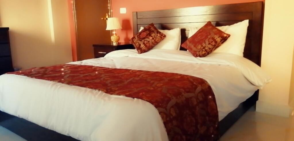 A neatly made bed with a white and red patterned bedspread, a wooden headboard, and two decorative pillows.