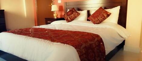A neatly made bed with a white and red patterned bedspread, a wooden headboard, and two decorative pillows.