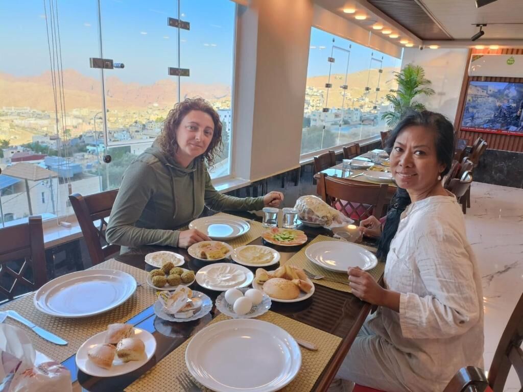 Un comedor con una mesa dispuesta para una comida, ventanas amplias con vistas a un paisaje urbano y un interior de restaurante con sillas y mesas.