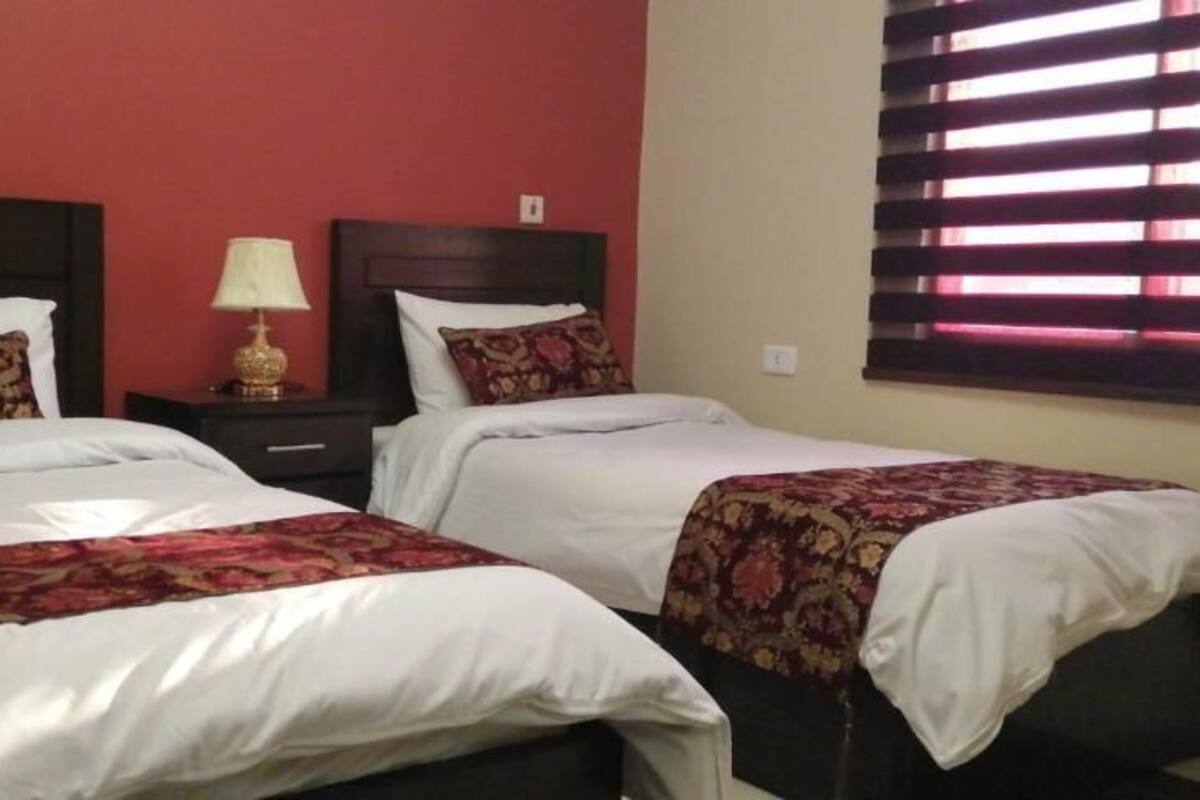 A double room with two beds, each with a floral bedspread and white pillows. There is a nightstand with a lamp between the beds.