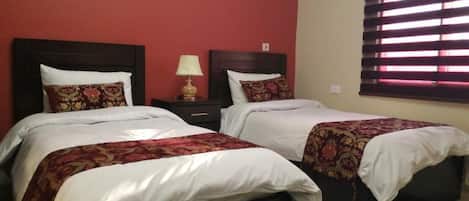 A double room with two beds, each with a floral bedspread and white pillows. There is a nightstand with a lamp between the beds.