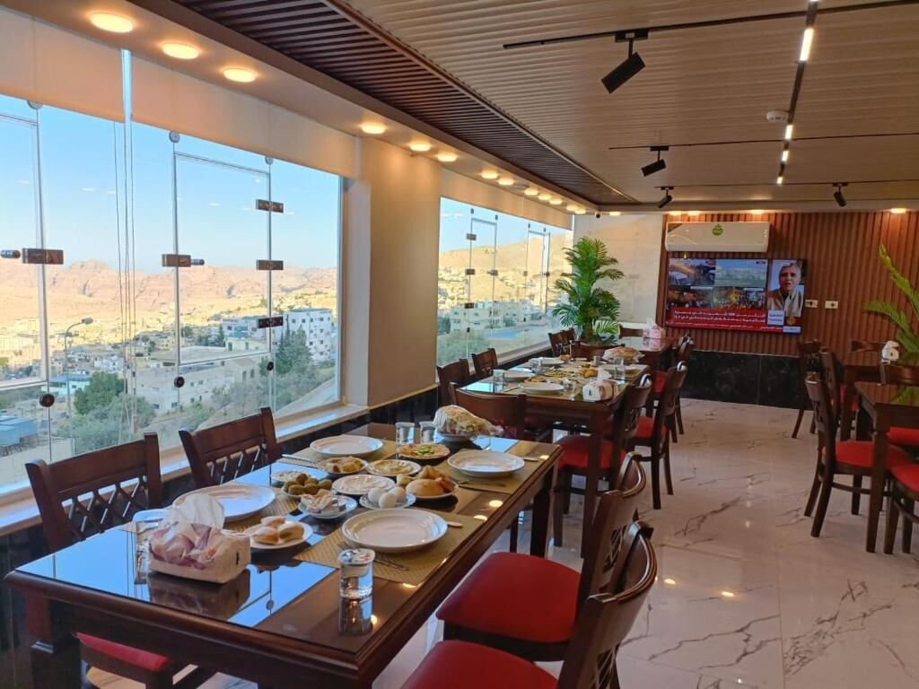 Un espace repas avec des tables dressées pour le repas, de grandes fenêtres offrant une vue sur le paysage urbain et un écran de télévision fixé au mur.
