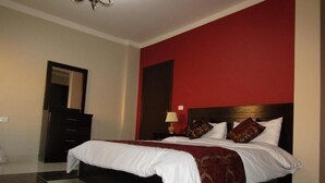 A hotel room with a large bed, a nightstand, a mirror, and a red accent wall. - Petra Crystal hotel (Wadi Musa)