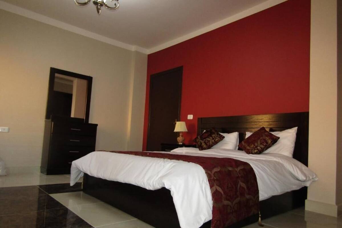 A hotel room with a large bed, a nightstand, a mirror, and a red accent wall.
