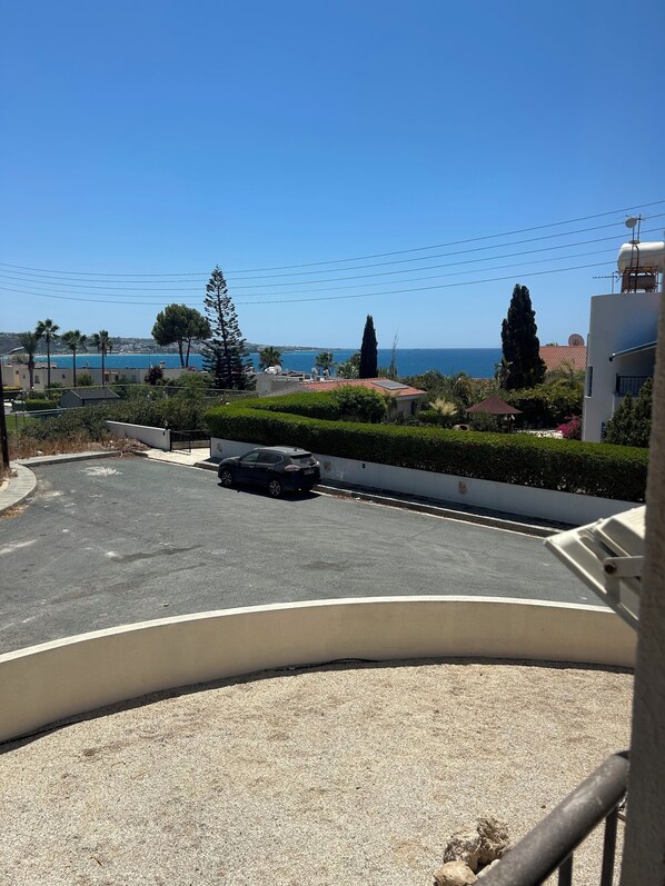 A parking area with a car, a building with a satellite dish, and a view of the sea.