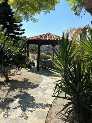 A covered patio area with a pergola, stone pathway, and surrounding greenery. - Coral Bay Family Villa | Private Pool | Walk to Restaurants, 3 Bedrooms.
 (Peyia)