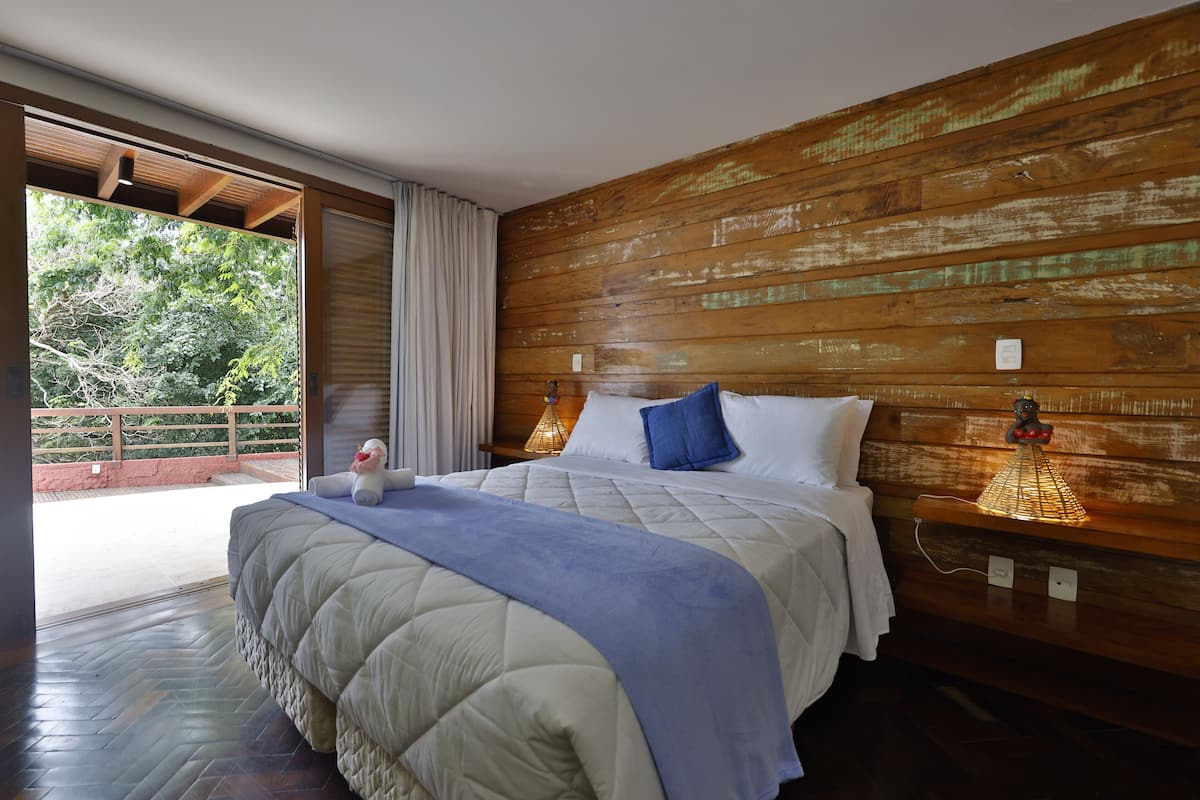 A bedroom with a large bed, wooden headboard, and a view of greenery outside.