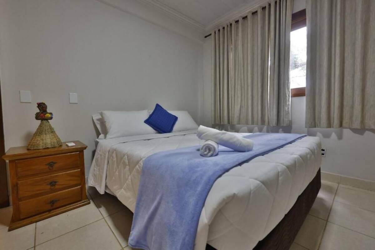 A hotel room with a bed, a wooden nightstand, and a window with curtains.