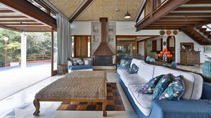 A spacious living room with a large sofa, a woven coffee table, and a fireplace. - Cap Ferrat Boutique Hotel (Búzios)