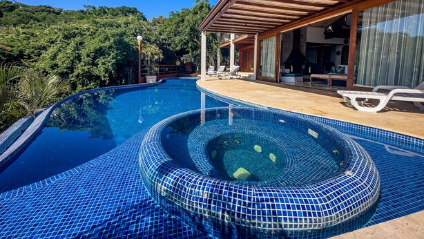 A swimming pool with a hot tub, surrounded by a wooden deck and a covered patio area. - Cap Ferrat Boutique Hotel (Búzios)
