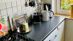 Una cocina con estufa a gas, lavadora, cafetera y ventana con vista a árboles.