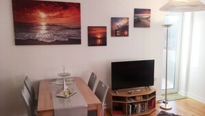 Una sala de estar con una mesa de comedor, sillas, un televisor de pantalla plana, una estantería y obras de arte en la pared que representan atardeceres.