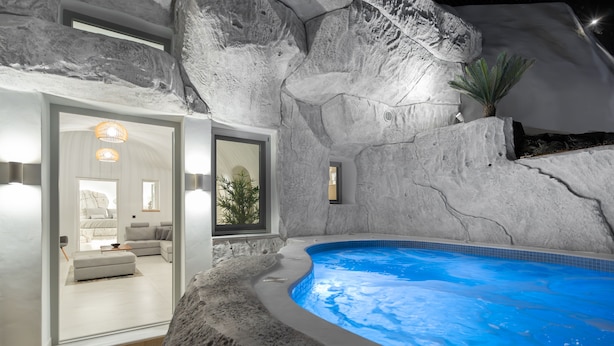 A modern indoor pool with a natural rock wall, a cozy seating area with a sofa and a coffee table, and a large window offering a view of the outside.