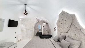 A modern bedroom with a large bed, a bathtub, and a stone wall arch.