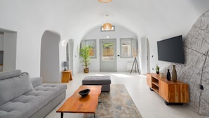 A modern living room with a grey sofa, wooden coffee table, and a TV mounted on a stone wall.