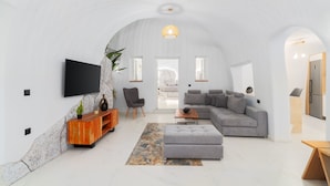 A spacious living room with a grey sectional sofa, a wooden entertainment unit, and a flat-screen TV mounted on the wall.