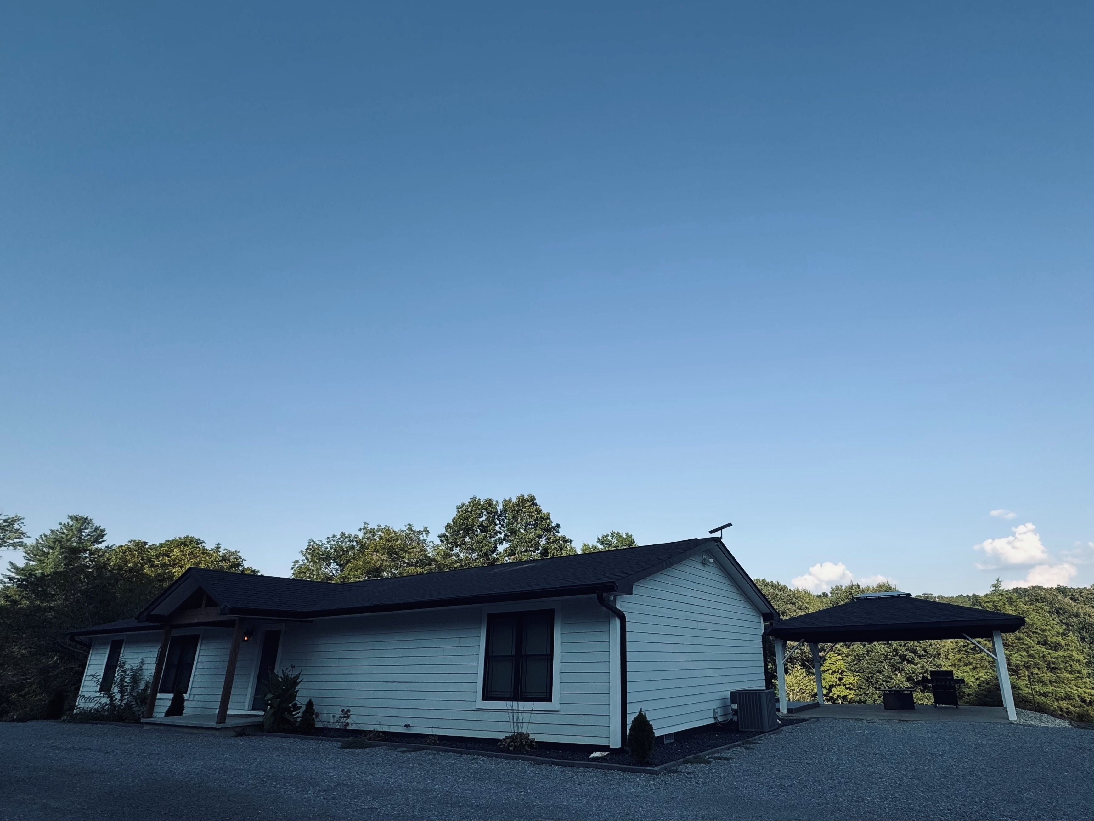 A single-story house with a covered porch, surrounded by trees and a clear sky.