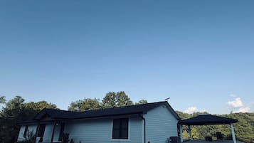 A single-story house with a covered porch, surrounded by trees and a clear sky.