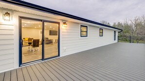 A modern house with a wooden deck, large sliding glass doors leading to a dining area, and a small attached garage.
