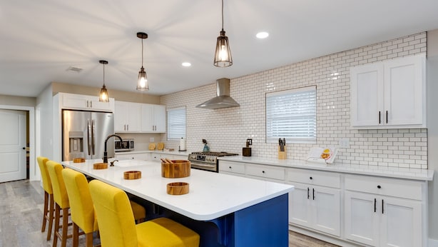 A modern kitchen with white cabinets, a large island with stools, and pendant lighting.