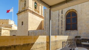 A stone building with a bell tower and a flag. - Stay inside the walls of Gozo Cittadella fortress (Ir-Rabat Għawdex)
