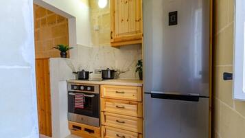 A compact kitchen with a built-in oven, a stainless steel refrigerator, wooden cabinets, and a marble backsplash.