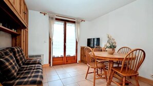 Ein Essbereich mit Holztisch und Stühlen, einer Couch und einem Fernseher an der Wand.