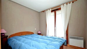 Ein Schlafzimmer mit einem hölzernen Bett, zwei Nachttischen mit Lampen, einem Fenster mit Vorhängen und einer Heizung.