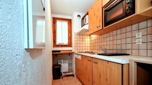 Eine kleine Küche mit Holzausstattung, einer Mikrowelle und einer gefliesten Spritzschutzwand.