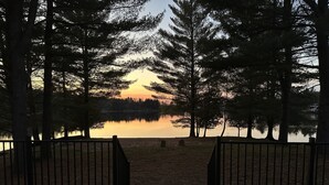 Une terrasse en bois avec une rambarde en métal, donnant sur un lac paisible, avec des arbres en arrière-plan.