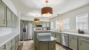 A modern kitchen with green cabinets, stainless steel appliances, and a central island.