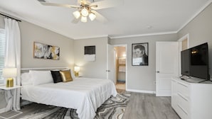 A bedroom with a bed, a ceiling fan, a TV, and a door leading to a bathroom.