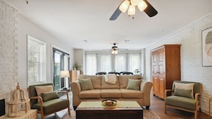 A living room with a beige sofa, two armchairs, a coffee table, and a ceiling fan.