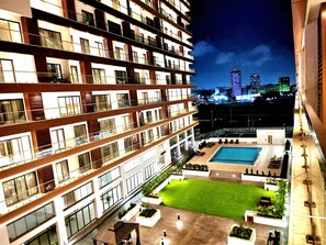 Um hotel com vários andares, piscina no terraço, gramado bem cuidado e vista para a cidade ao fundo.