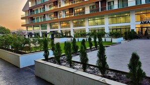 A multi-story hotel with a modern design, featuring balconies, large windows, and a landscaped courtyard with young trees.