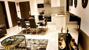 A modern kitchen with white cabinets, a built-in oven, and a microwave. There is a dining area with a glass table and chairs, and a rug on the floor.
