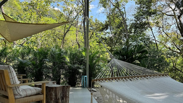 A hammock set up between trees, wooden chairs, and a small table in a garden area. - Amaj Eco Lodge (Sámara)